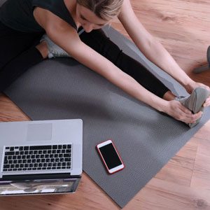 Remote physiotherapy, a woman exercising on the floor looking at her laptop and mobile phone.