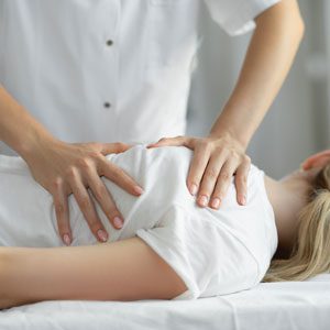 A female osteopath giving treatment to a patient by putting hands on the patient back.
